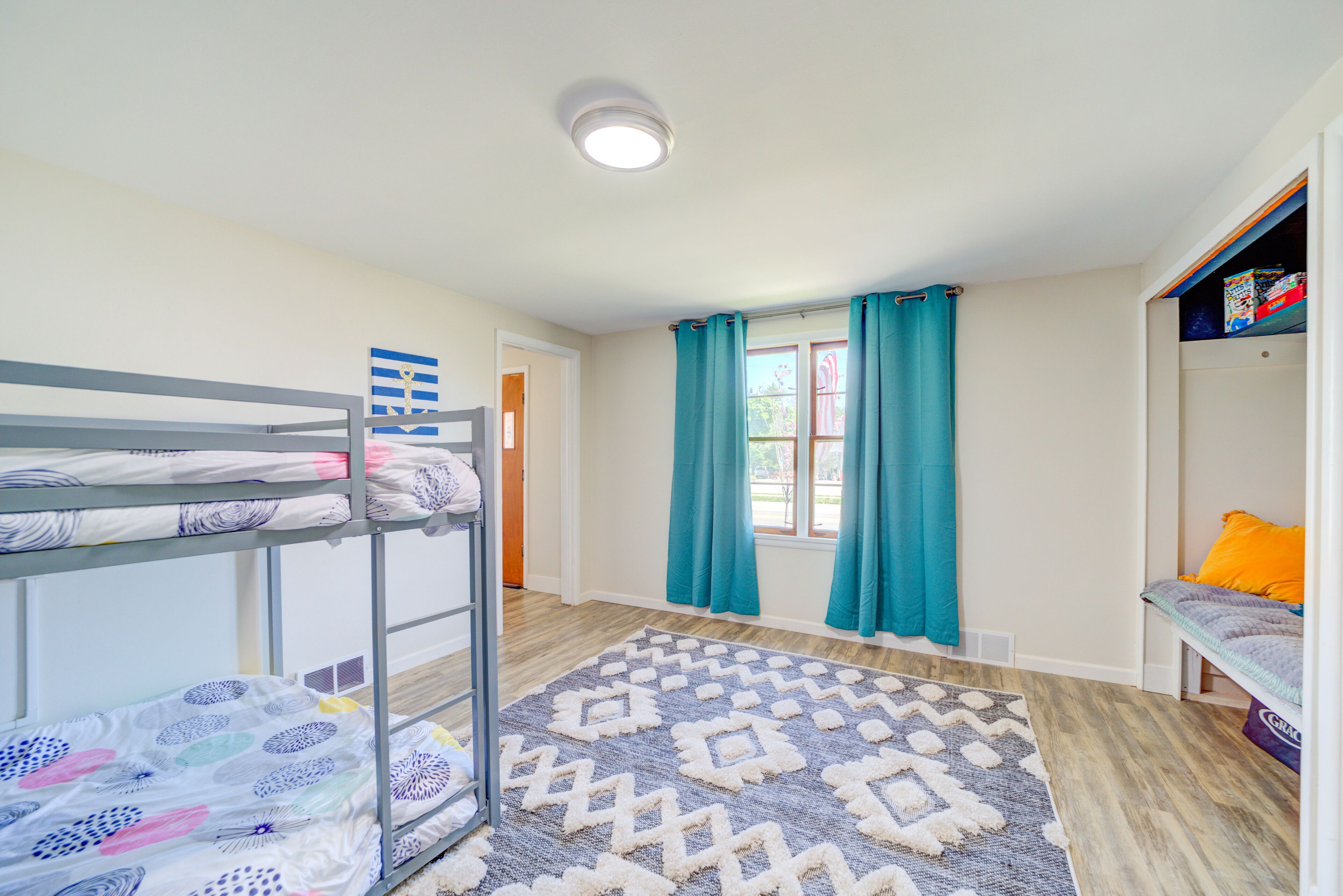 Dormitorio con literas, alfombra estampada, cortinas color turquesa y una ventana con vistas.