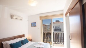 A bedroom with a bed, pillows, a nightstand, an air conditioner, a picture, and a balcony with a railing. - Villa Meena, 2BDR Kapparis Villa with Private Pool, Close to the Beach (Paralimni)