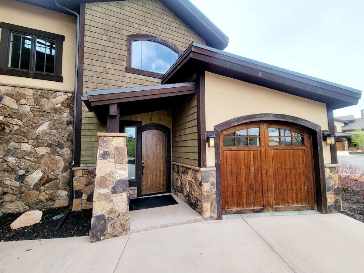 Une maison moderne avec une façade en pierre, une porte d’entrée en bois et une porte de garage.