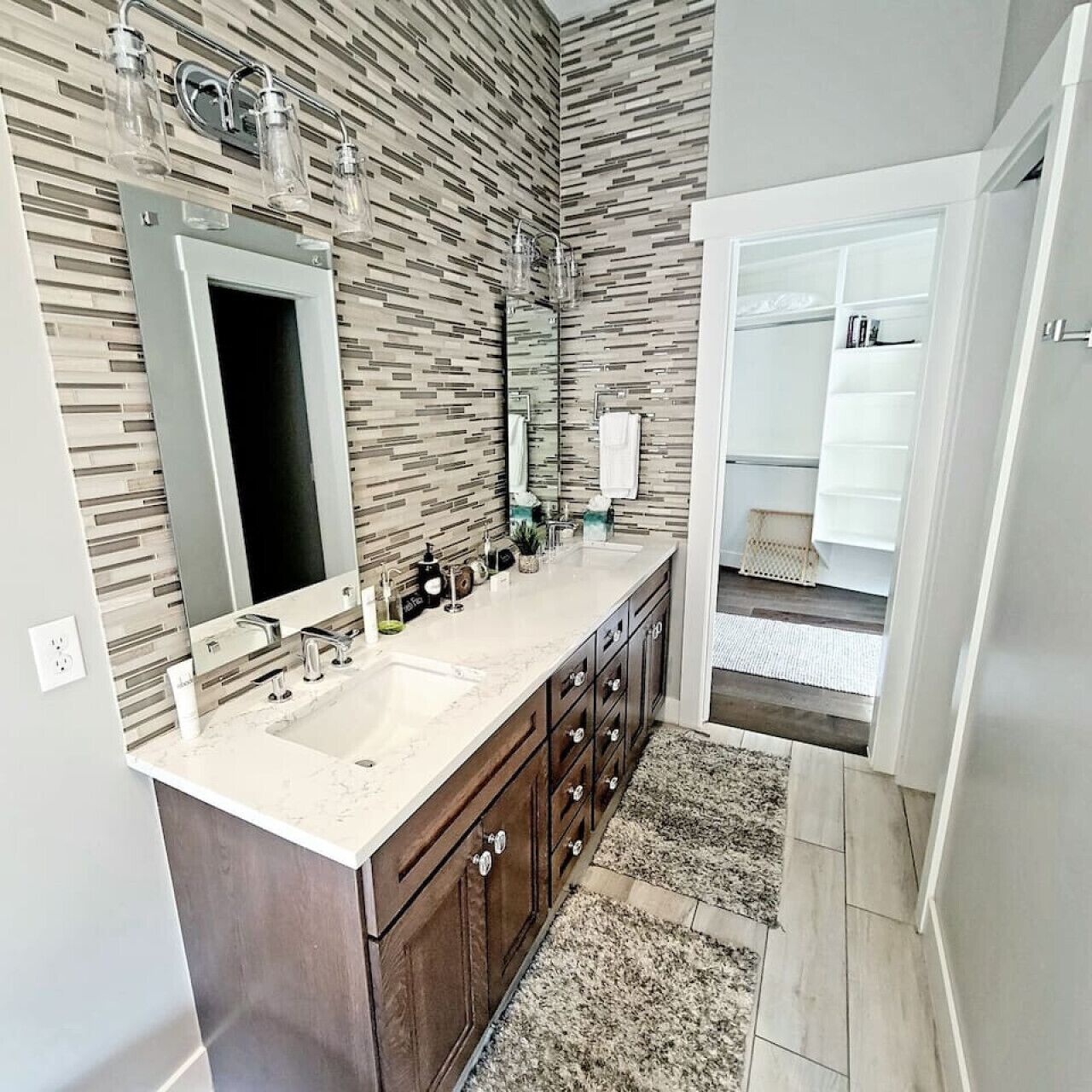 A modern bathroom with a double sink vanity, a large mirror, and a patterned wall.