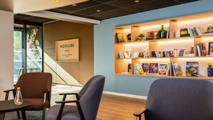 A hotel lobby with a reception desk, seating area, and a bookshelf with books and decorative items. - Mercure Toulouse Aéroport Blagnac (Blagnac)
