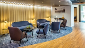 A modern lounge area with a curved wooden floor, blue sofas, and a small table with a plant. - Mercure Toulouse Aéroport Blagnac (Blagnac)