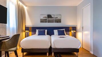 A hotel room with two beds, a desk, a chair, and a TV.