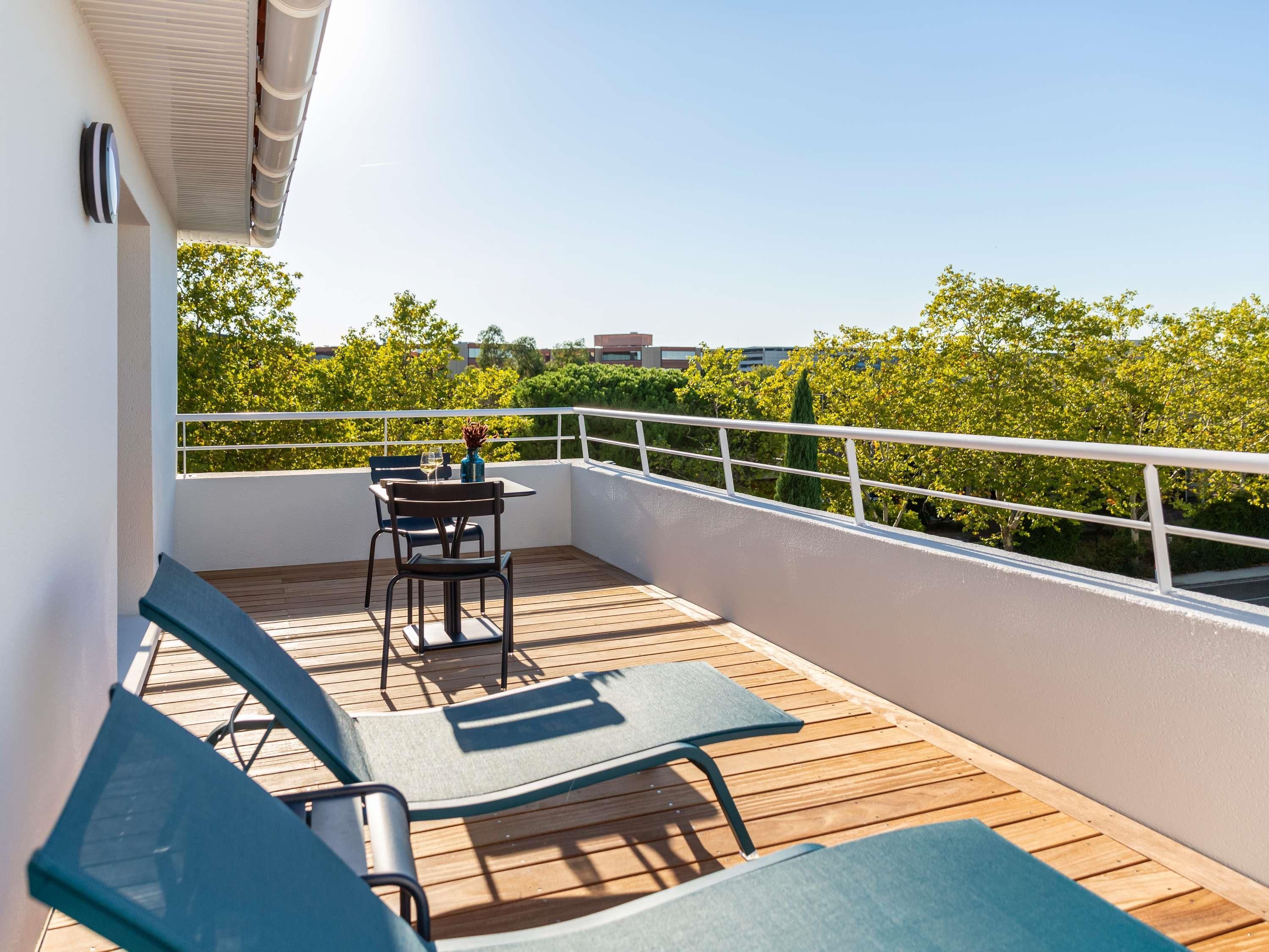 A balcony with a table and chairs, a railing, and a view of greenery.