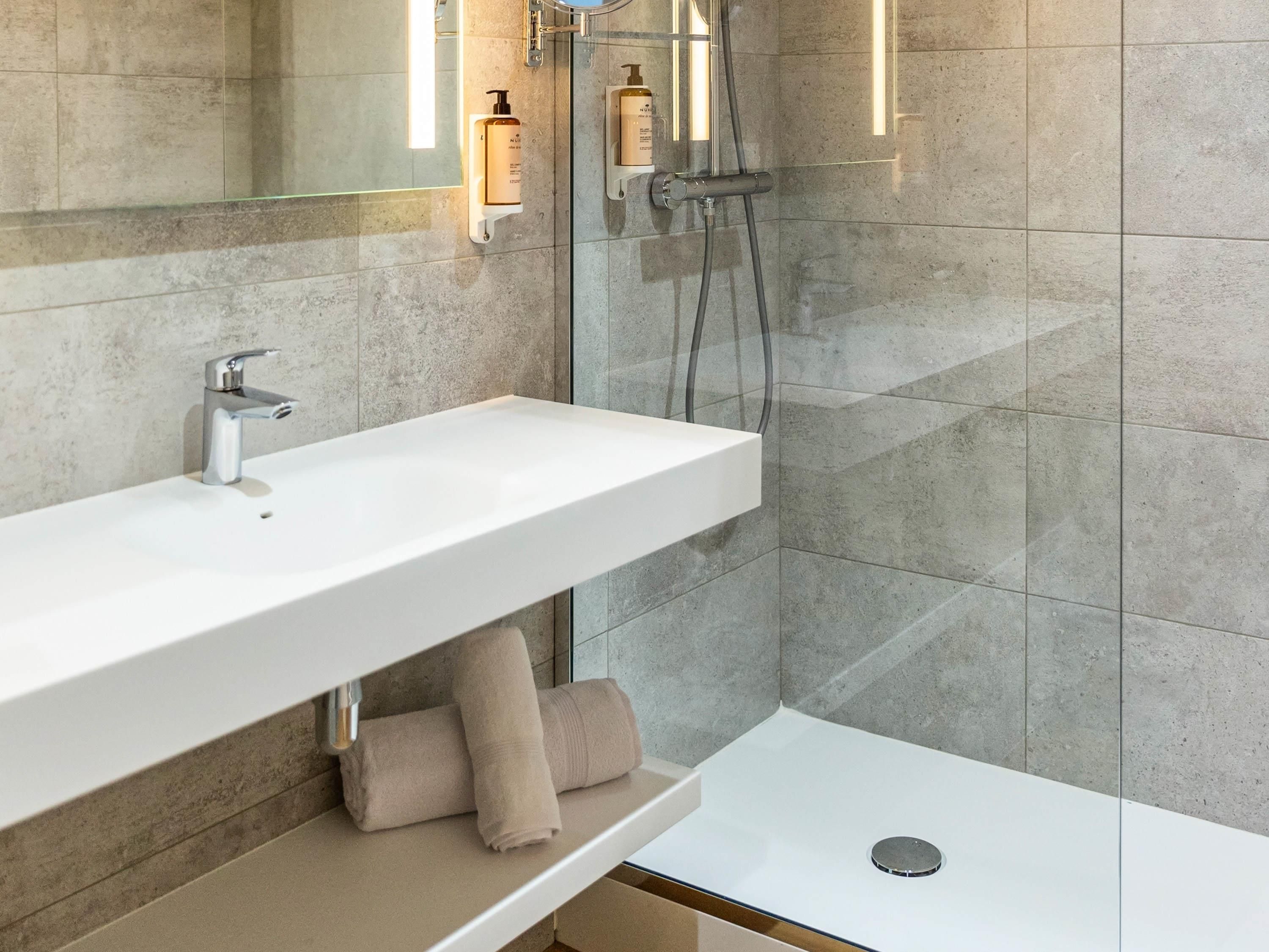 A modern bathroom with a white sink, a mirror, a towel rack, and a shower area.