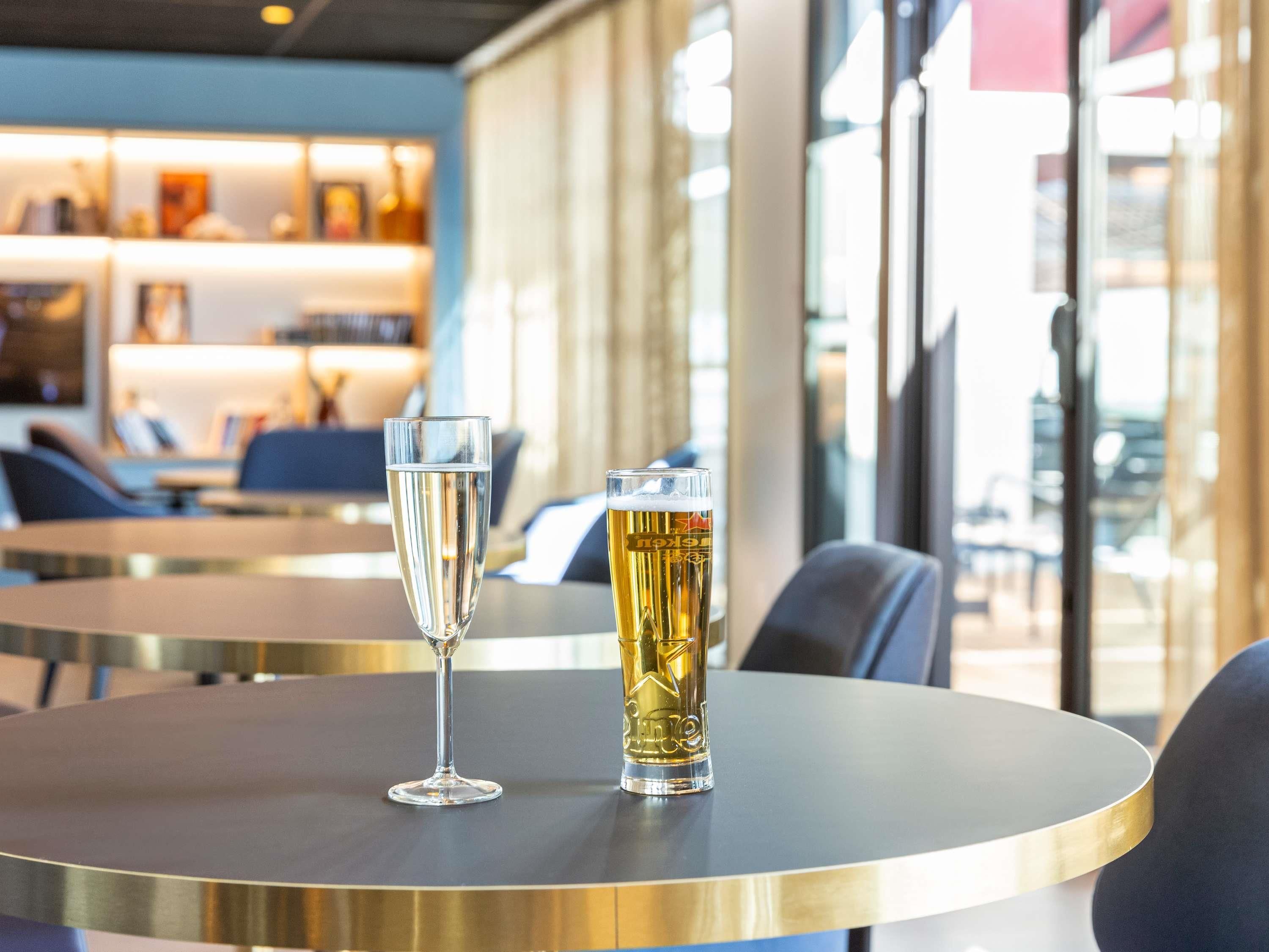 Two glasses on a table in a well-lit indoor setting with modern furniture and large windows.