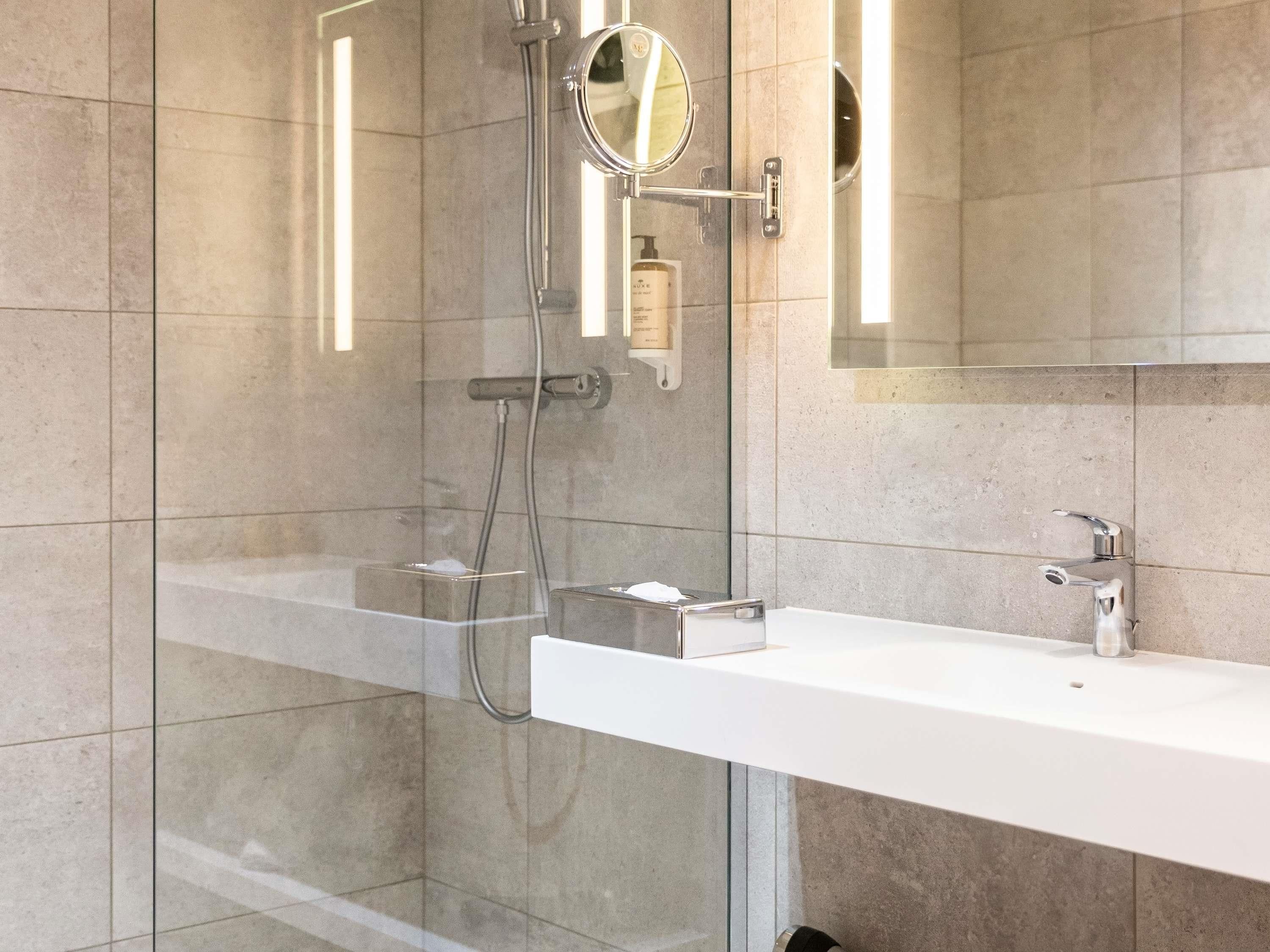 Un baño moderno con ducha de vidrio, un lavamanos blanco y un espejo con marco redondo.