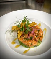 Un plato blanco con una porción de salmón ahumado, verduras verdes y una guarnición de microgreens.