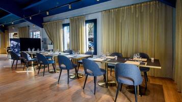 A modern dining area with wooden flooring, blue chairs, and tables set for dining.