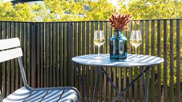 A round table with a vase and two glasses on it, a chair, and a metal fence in the background.