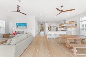 A spacious living area with a sofa, a wooden dining table, and a kitchen with white cabinetry and a central island.