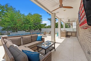A covered outdoor area with a pool, lounge chairs, a barbecue area, and a ceiling fan.
