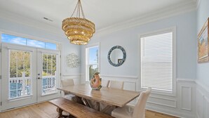 Comedor con mesa de madera, sillas blancas tapizadas, un banco y una lámpara decorativa.