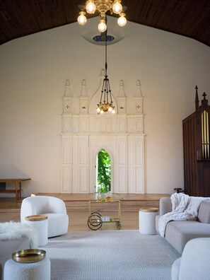A spacious room with a high ceiling, a large arched window, and a chandelier.