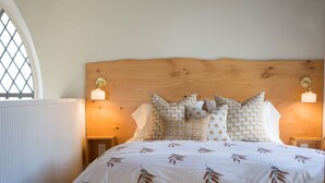 Ein Schlafzimmer mit einem hölzernen Kopfteil, einer zudeckenden Bettdecke mit Blumenmuster und zwei Nachttischlampen.