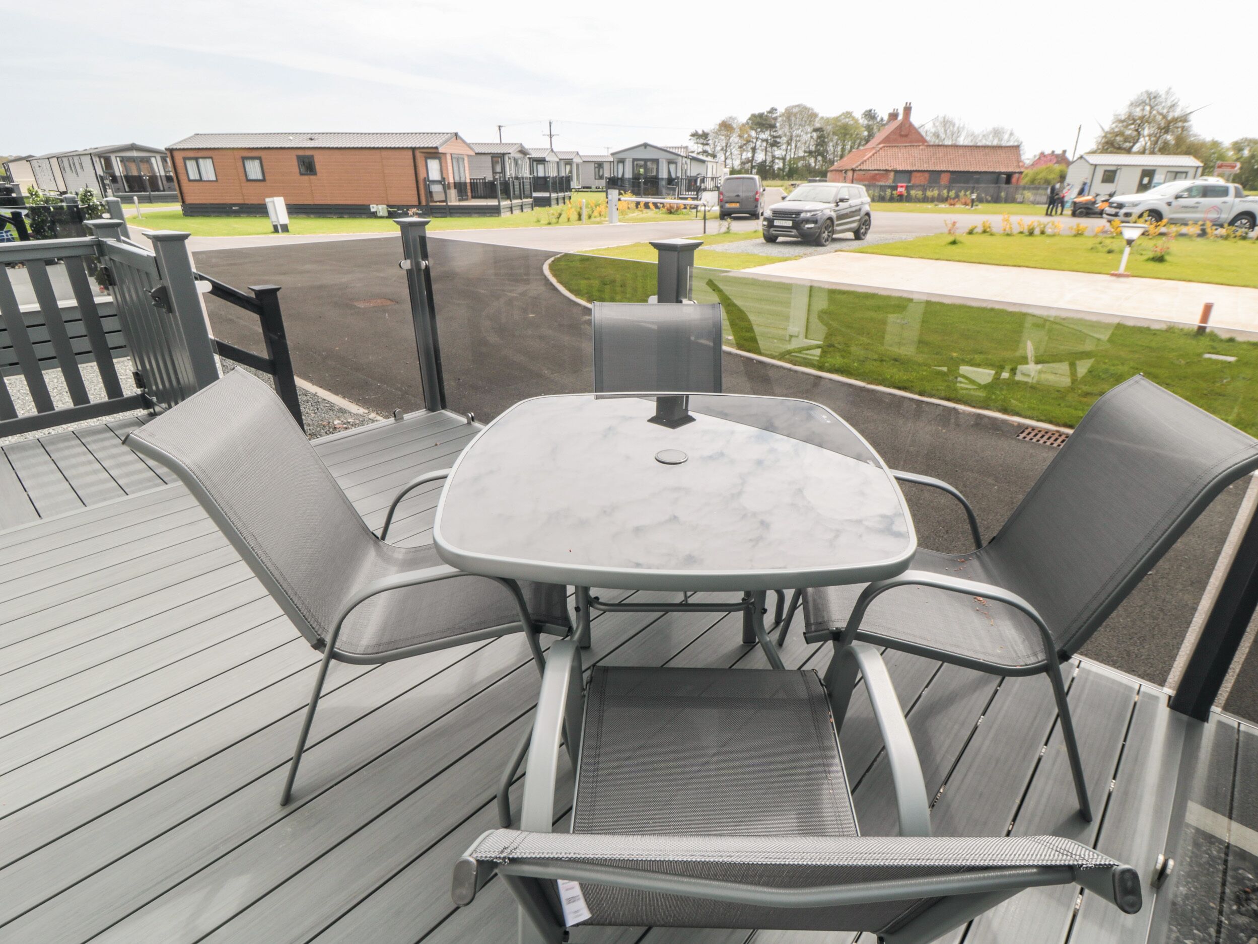 An outdoor patio with a table and chairs, a wooden deck, and a view of a street with buildings and cars.
