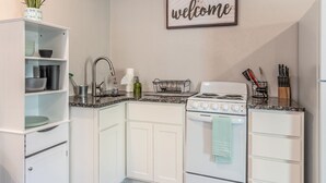 Une cuisine avec des meubles blancs, une cuisinière et un évier. Un panneau indiquant « Bienvenue » est accroché au mur.