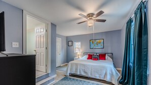 Une chambre à coucher avec un lit, un ventilateur de plafond, une table de chevet, une lampe et une carte accrochée au mur.