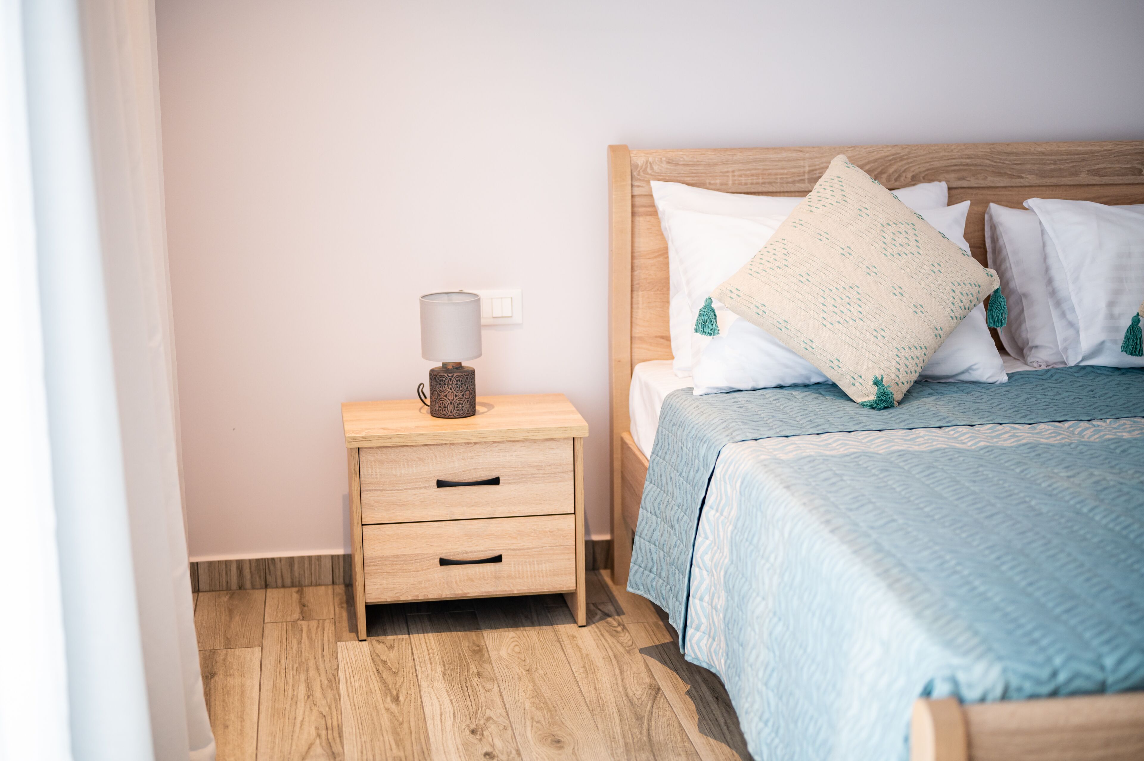 A bedroom with a wooden headboard, a bed with a blue quilt, a nightstand with a lamp, and a wall socket.