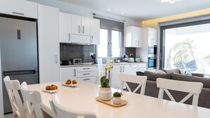 A modern kitchen with white cabinetry, a dining table with chairs, and a view of the outdoors through a sliding glass door. - beach deluxe house  (Kos)