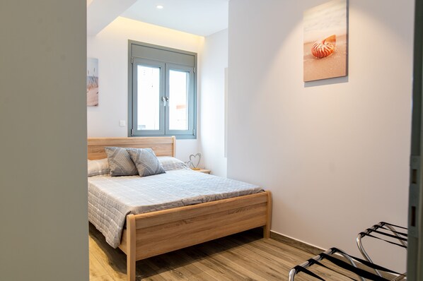 A bedroom with a wooden bed, a window with blinds, a wall-mounted artwork, and a wooden floor. - beach deluxe house (Kos)