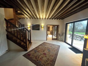 Una habitación con escalera de madera, alfombra estampada y vista a un espacio exterior con mesa y sillas.