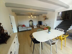 Una sala de estar moderna con comedor, una escalera y un televisor al fondo.