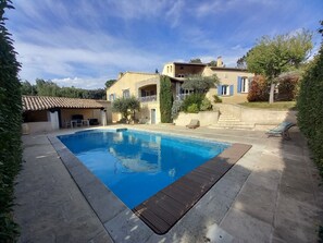 Una piscina con borde de baldosas, una zona de estar techada y un edificio de piedra con balcón.