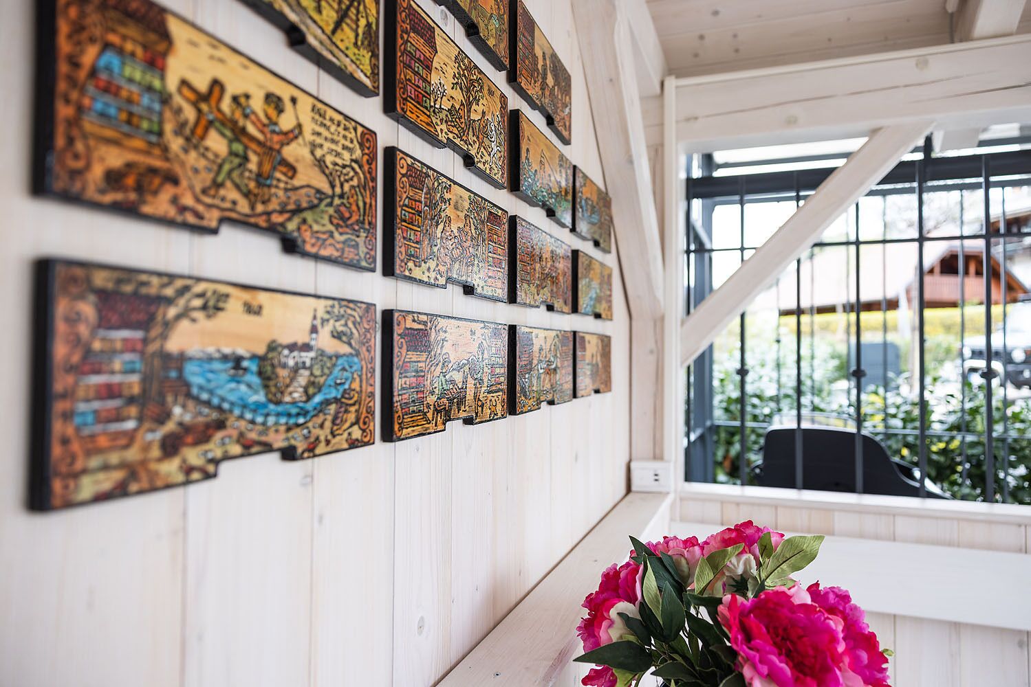 A wall with multiple framed artworks and a window with a view of greenery.
