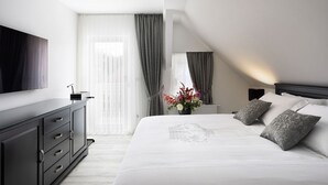Ein modernes Hotelzimmer mit einem großen Bett, einem flachbildfernseher an der Wand, einer dunklen Holzkommode und einem Fenster mit transparenten Vorhängen.