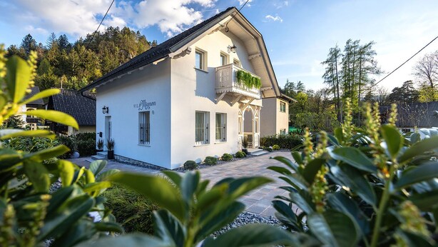 Ein zweistöckiges Haus mit weißer Fassade, einem Balkon und einem Vorgarten.