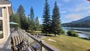 Um deck com móveis de exterior, lareira e vista para um rio e floresta.