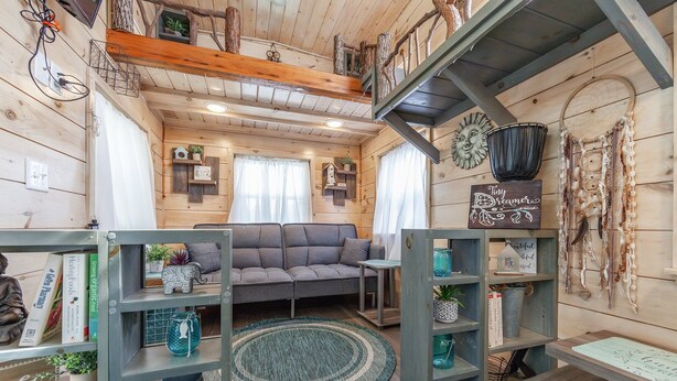 Ein gemütliches Blockhauss-Interieur mit einem grauen Sofa, Holzregalen mit verschiedenen Dekorationen und einer rustikalen Decke.