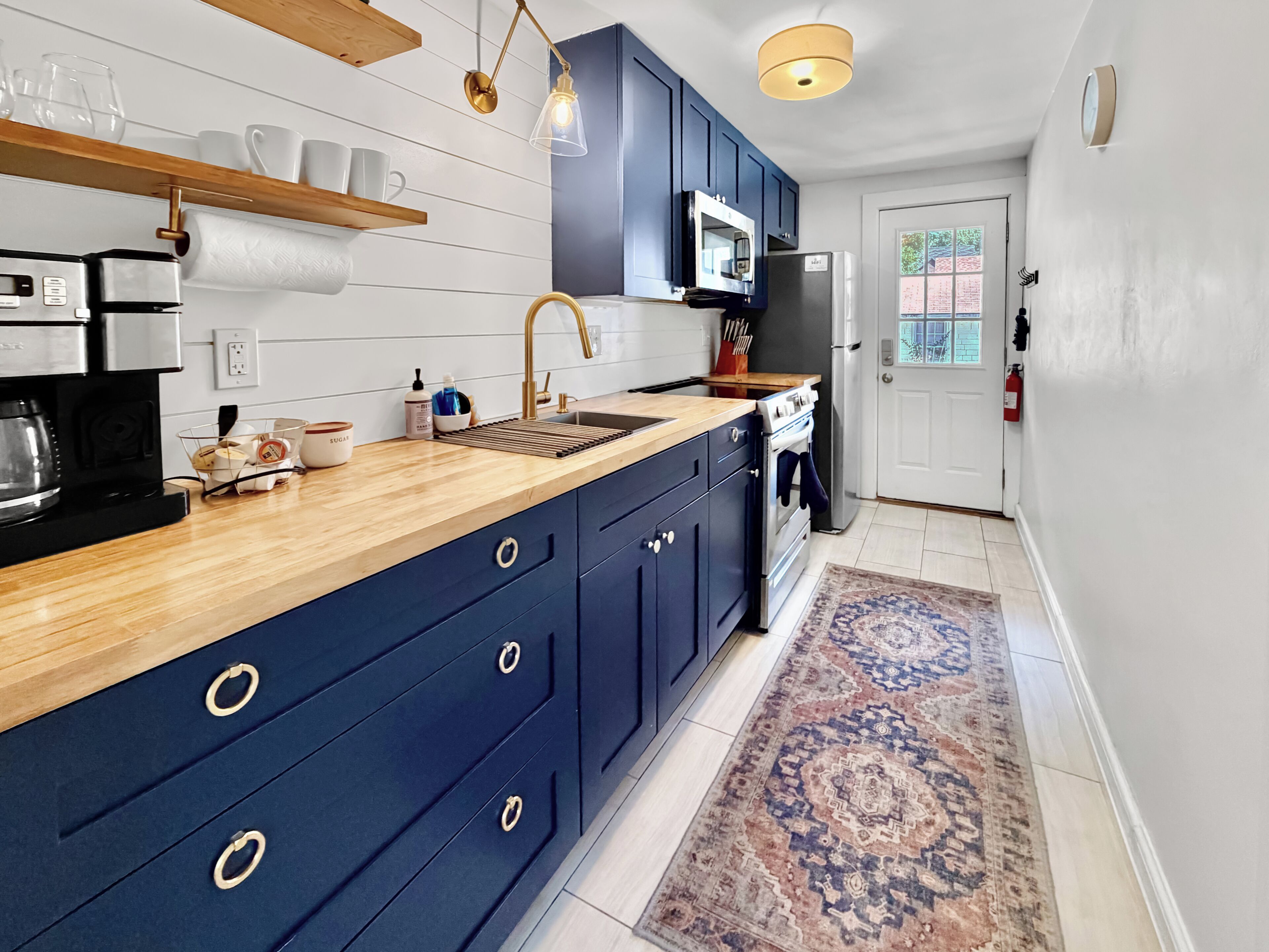 Eine moderne Küche mit dunkelblauen Schränken, einer Holz Arbeitsplatte, einem eingebauten Ofen und einem Edelstahl-Kühlschrank.