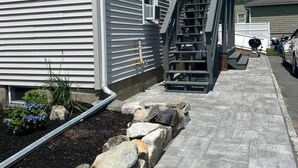 Un immeuble résidentiel à l’extérieur gris, avec un escalier apparent menant à l’entrée et un chemin pavé bordé de pierres.