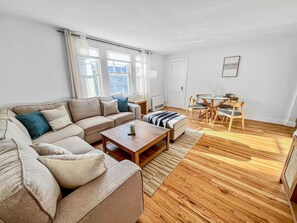 A living room with a sofa, coffee table, and a dining area with chairs. - Willard By the Sea - 30 ft to the beach- 1st floor (South Portland)