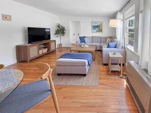 A modern living room with a flat-screen TV, sofa, ottoman, and a coffee table. - Willard By the Sea - 30 ft to the beach (South Portland)