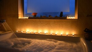 Una bañera con ventana, velas y una planta pequeña.
