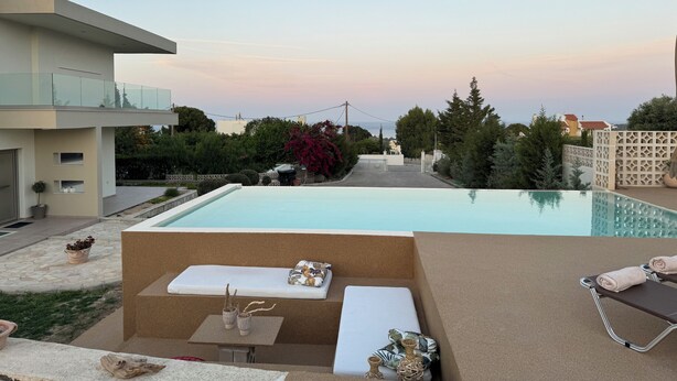 Un área moderna junto a la piscina con una silla de descanso, una mesita con adornos y vistas del barrio circundante.