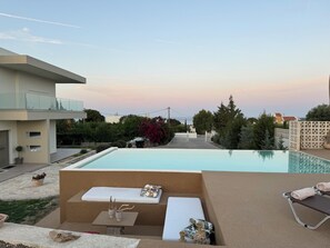 Un espace moderne aménagé au bord de la piscine, comprenant un fauteuil de relaxation, une petite table agrémentée d’objets décoratifs et offrant une vue sur le quartier environnant.