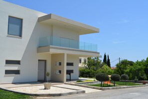 Un bâtiment moderne à deux étages, doté d’un balcon, d’une porte et d’un petit jardin agrémenté de plantes en pot.