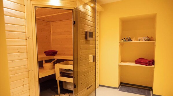 Una sala de sauna con paredes de madera, una puerta de vidrio y un estante con toallas y botellas.
