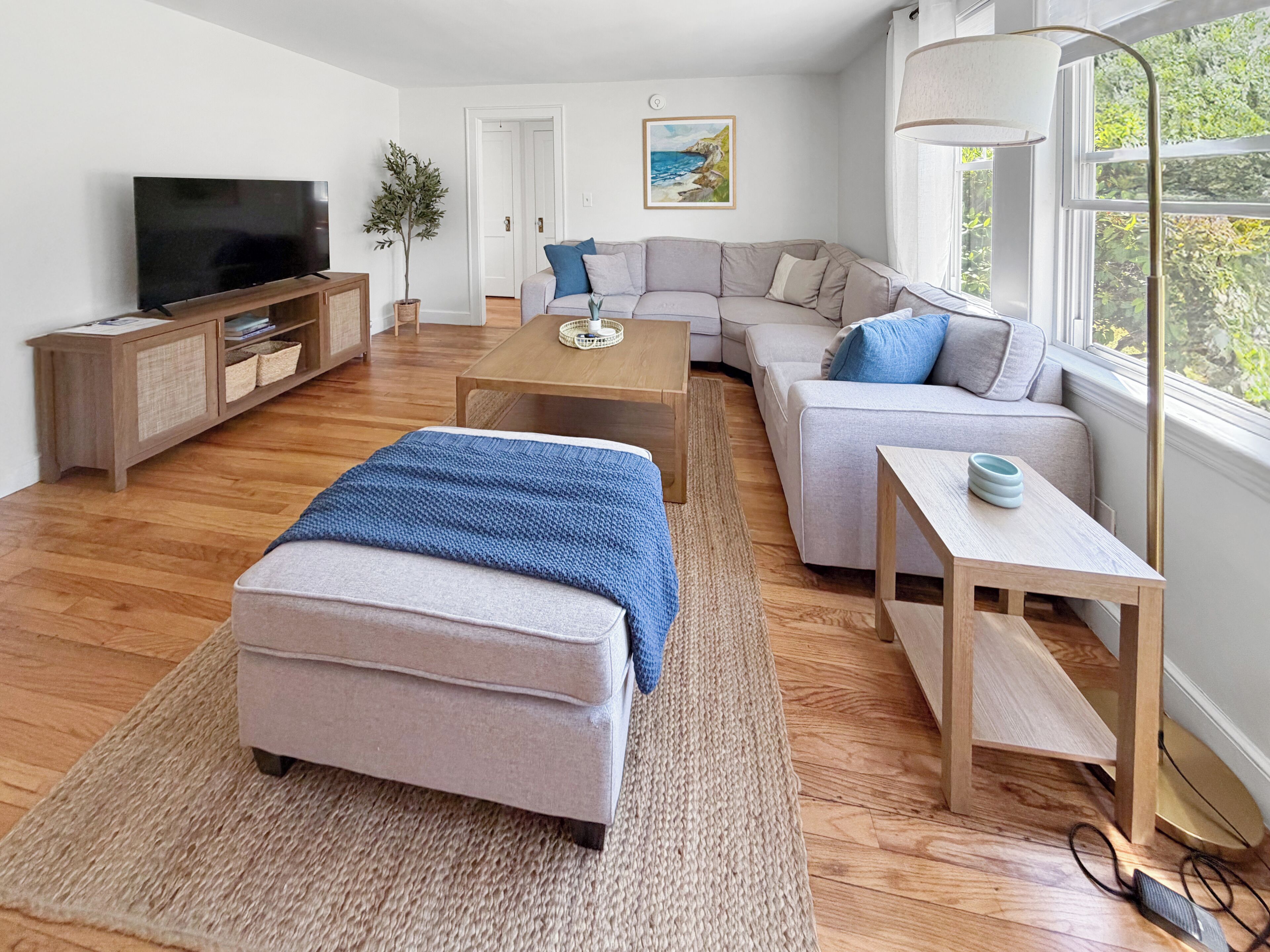 Un salon moderne comprenant un canapé, un pouf, une table basse, un téléviseur et une lampe.