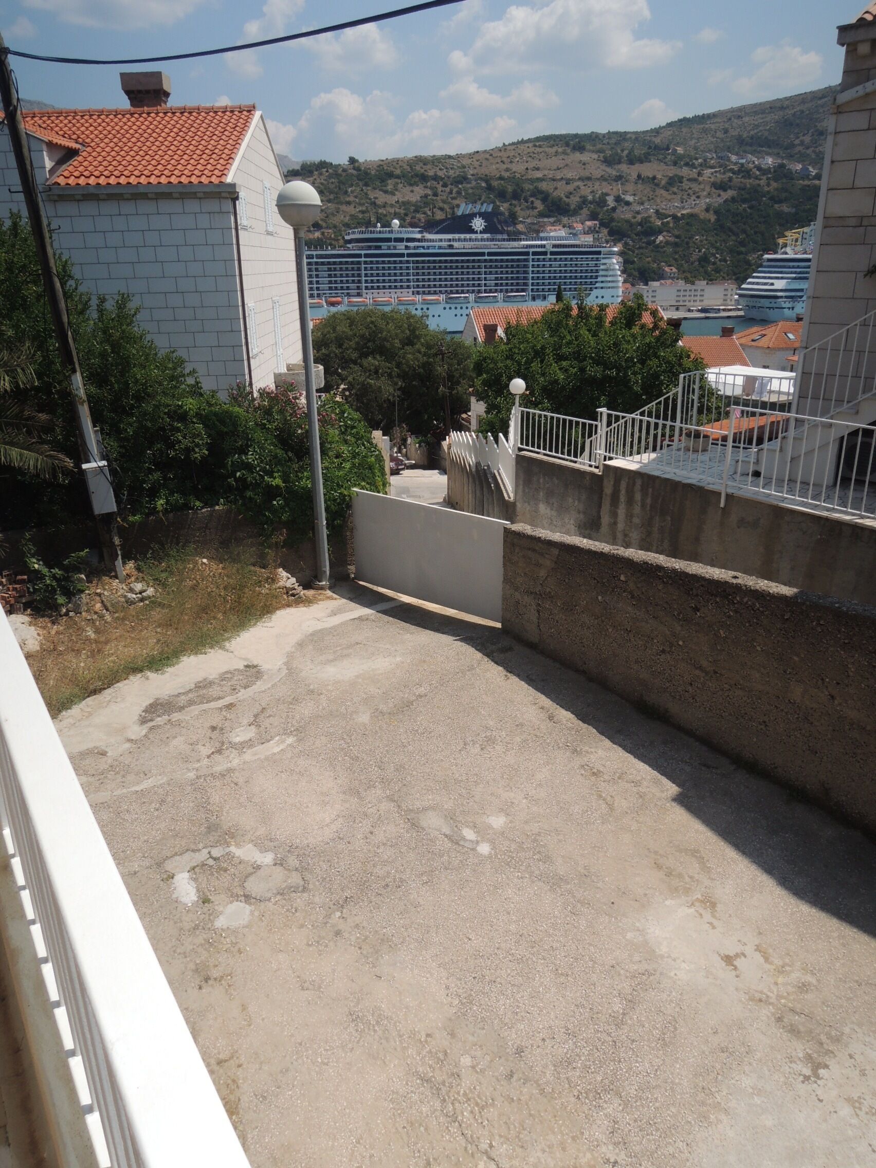 Vista de una zona residencial con una calle pavimentada, un edificio blanco con techo de tejas rojas y una vista distante de cruceros.