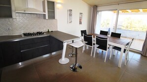A modern kitchen with a gas stove, white cabinets, and a dining area with a table and chairs. - Three-room apartment Le Maree 8 with sea view (Cannigione)