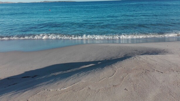 A beach with clear blue water, a sandy shore, and a distant mountain. - Three-room apartment Le Maree 8 with sea view (Cannigione)