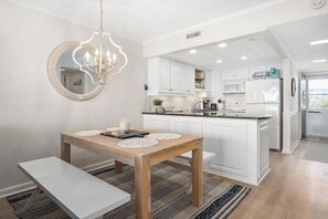 Una cucina moderna con mobili bianchi, un tavolo da pranzo in legno con sottopiatti, una panca e un lampadario.