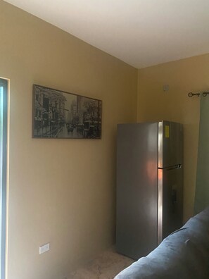 Une pièce avec un mur de couleur beige, un grand réfrigérateur et un tableau représentant un paysage urbain.