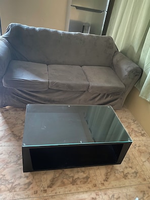 Une piÚce avec un canapé gris et une table basse en verre, le tout posé sur un sol en marbre.