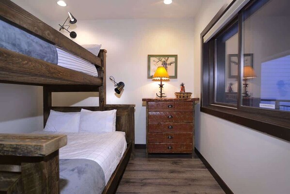A bunk bed with a wooden headboard, a wooden dresser with drawers, a lamp, and a framed picture on the wall.
